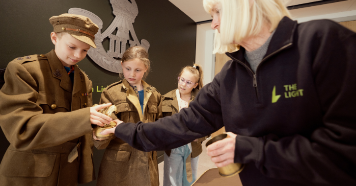 Children dressed in historic military uniform uniforms handling objects from the DLI exhibition at The Light, Durham.